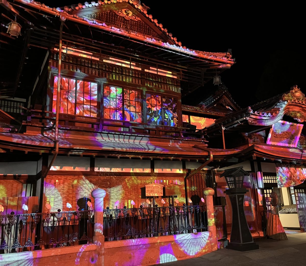 夜の道後温泉本館。プロジェクションマッピングで建物いっぱいに花の模様が映し出されている